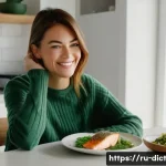 Home 21 우울증과 관련된 음식의 역할 - A woman in her early 30s, with a warm, gentle smile, is sitting at a light-filled kitchen table. She...